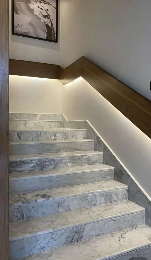 Escalier intérieur en marbre veiné clair, main courante en bois et éclairage LED